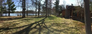 Une cabane aux murs en pierre, entourée de grands arbres et bordée par un lac.