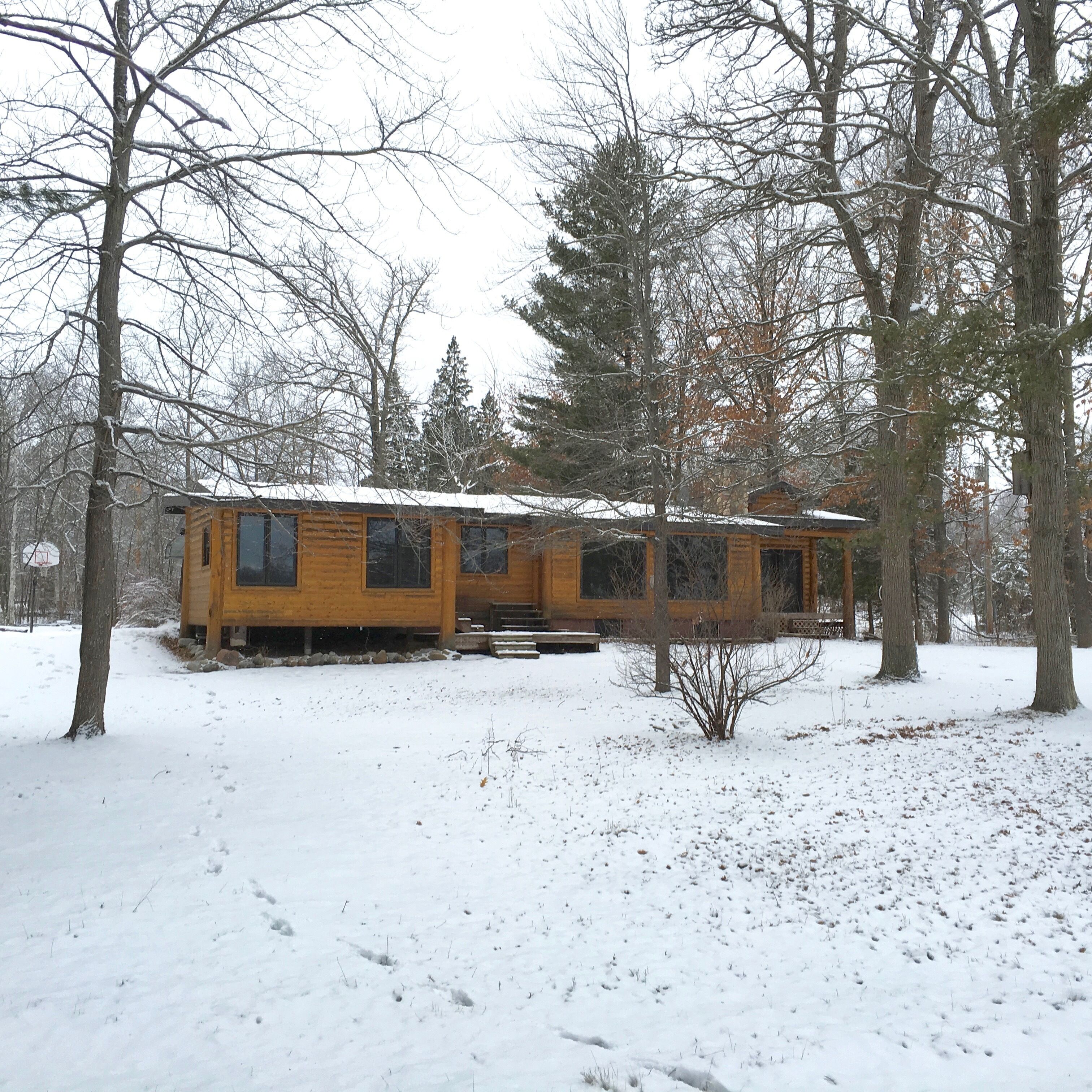 Une cabane aux murs en bois, entourée d’un paysage enneigé et d’arbres.