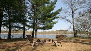 Ein Campingplatz mit zwei Stühlen vor einem Lagerfeuer, umgeben von Bäumen und einem See.