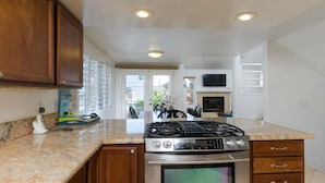 A kitchen with a gas stove, oven, wooden cabinets, granite countertops, and a view of the living area with a fireplace and TV. - 3 bdr, 3 bath Home  Walk to bay, ocean, restaurants and shops! (San Diego)
