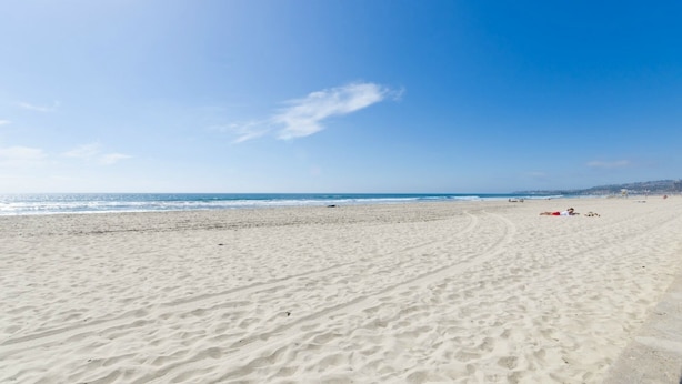 A wide sandy beach with gentle waves, a clear sky, and a distant shoreline with buildings. - 3 bdr, 3 bath Home  Walk to bay, ocean, restaurants and shops! (San Diego)