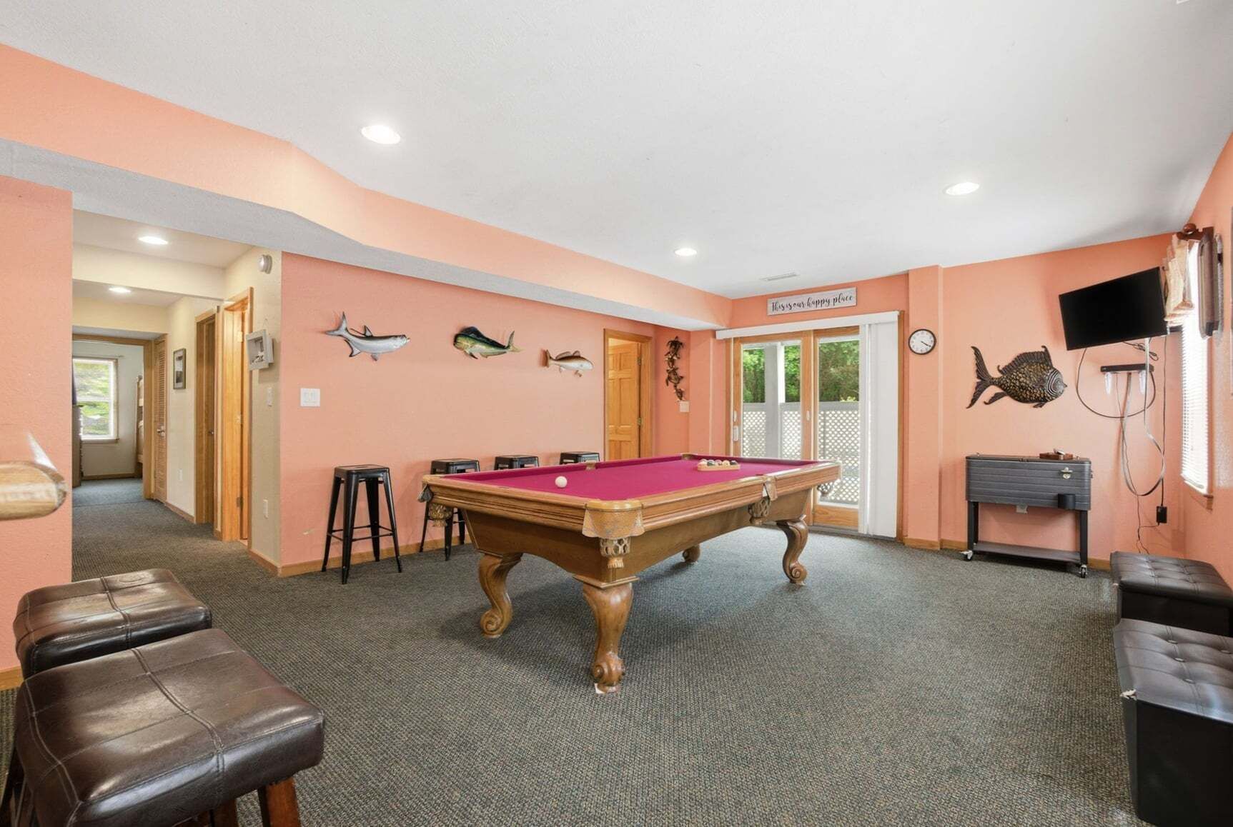 A pool table in a room with peach walls, a clock, and fish decorations.