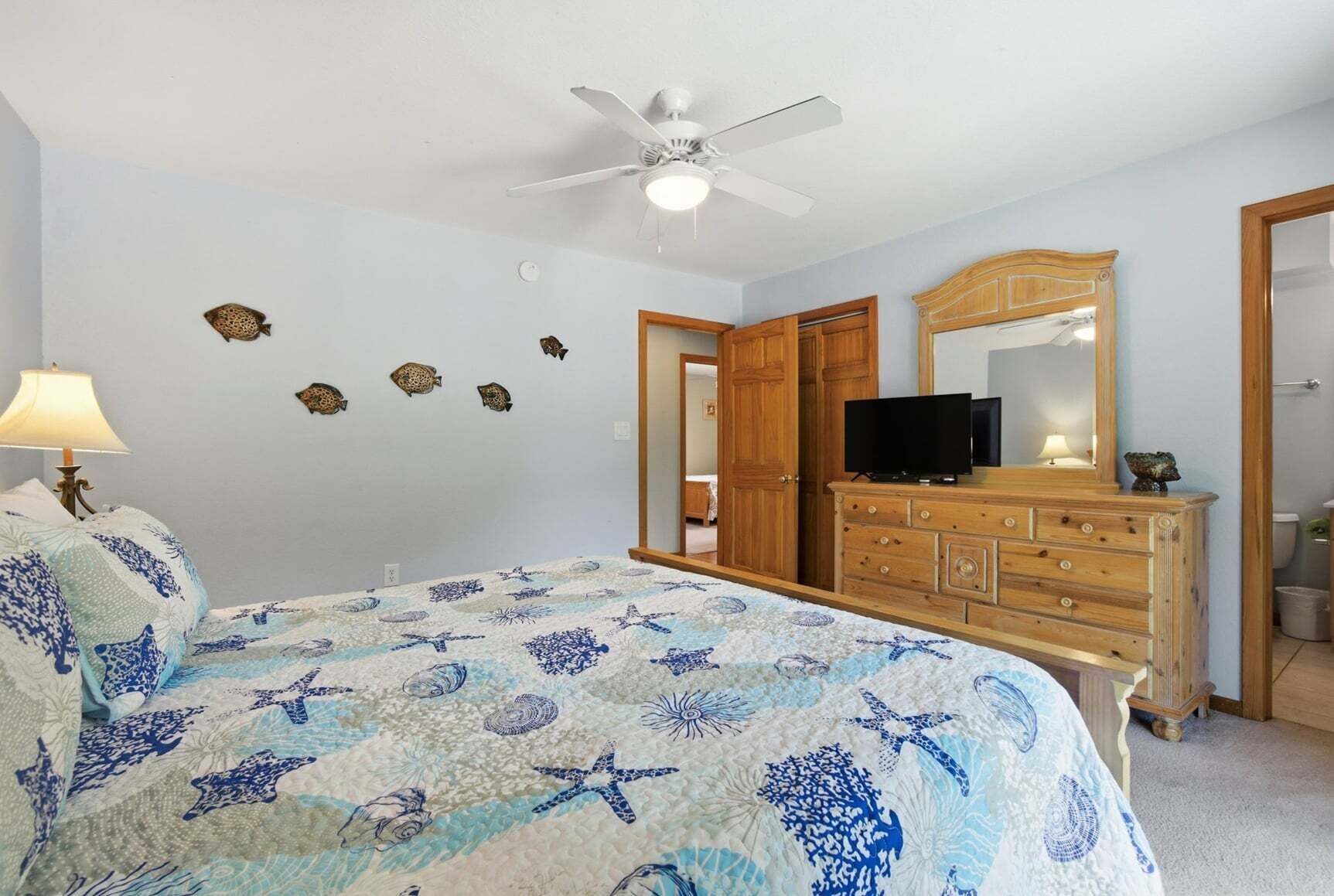 A bedroom with a bed, dresser, television, ceiling fan, and wall decorations.