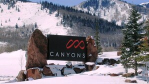 A sign with the word "CANYONS" and a red infinity symbol, surrounded by snow-covered rocks and trees. - Rustic Mountain Charm at The Canyons (Park City)