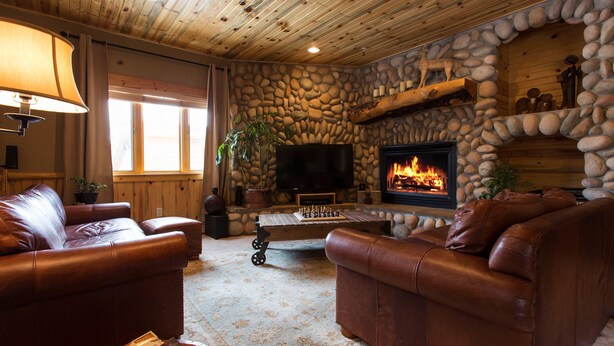 A cozy living room with leather sofas, a stone fireplace, a flat-screen TV, and a chess table. - Rustic Mountain Charm at The Canyons (Park City)