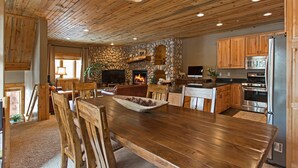 A spacious wooden dining area with a stone fireplace, modern kitchen with stainless steel appliances, and a rustic ceiling design. - Rustic Mountain Charm at The Canyons (Park City)