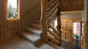 A wooden staircase with a carpeted landing, wooden walls, and a window with a view of snow-covered trees. - Rustic Mountain Charm at The Canyons (Park City)