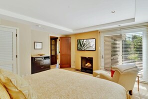 A bedroom with a large bed, a fireplace, a desk, and a chair.