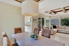 A modern living room with a dining area, a sofa set, and a large window providing a view of the outdoors. - Desert Luxe | 3BR Santa Rosa Cove (La Quinta)