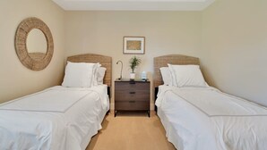 Ein Schlafzimmer mit zwei Einzelbetten, einem Schminktisch, einem runden Spiegel und einem gerahmten Bild an der Wand.