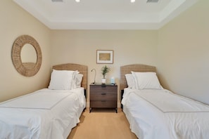 A bedroom with two single beds, a dresser, a round mirror, and a framed picture on the wall. - Desert Luxe | 3BR Santa Rosa Cove (La Quinta)
