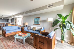 A modern living room with a blue sofa set, a glass coffee table, and a large potted plant.