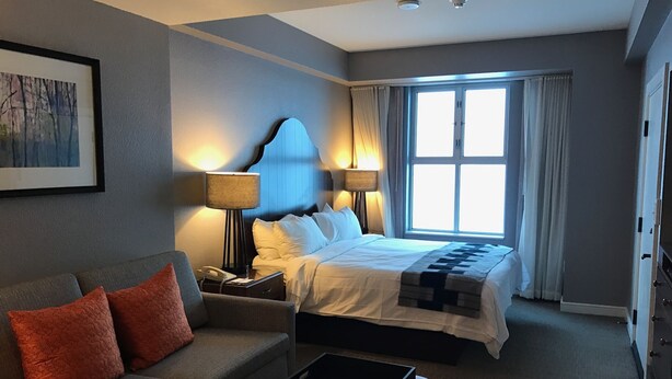 Een hotelkamer met een bed, een slaapbank, een nachtkastje met lamp en een raam met gordijnen.