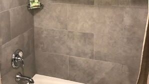 Een badkamer met grijze tegels, een douche, een bad en een plank met toiletartikelen.