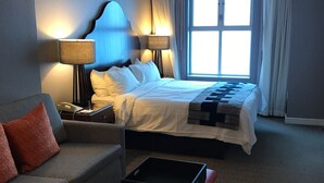 Een hotelkamer met een bed, een bank, een nachtkastje, een lamp en een raam met gordijnen.