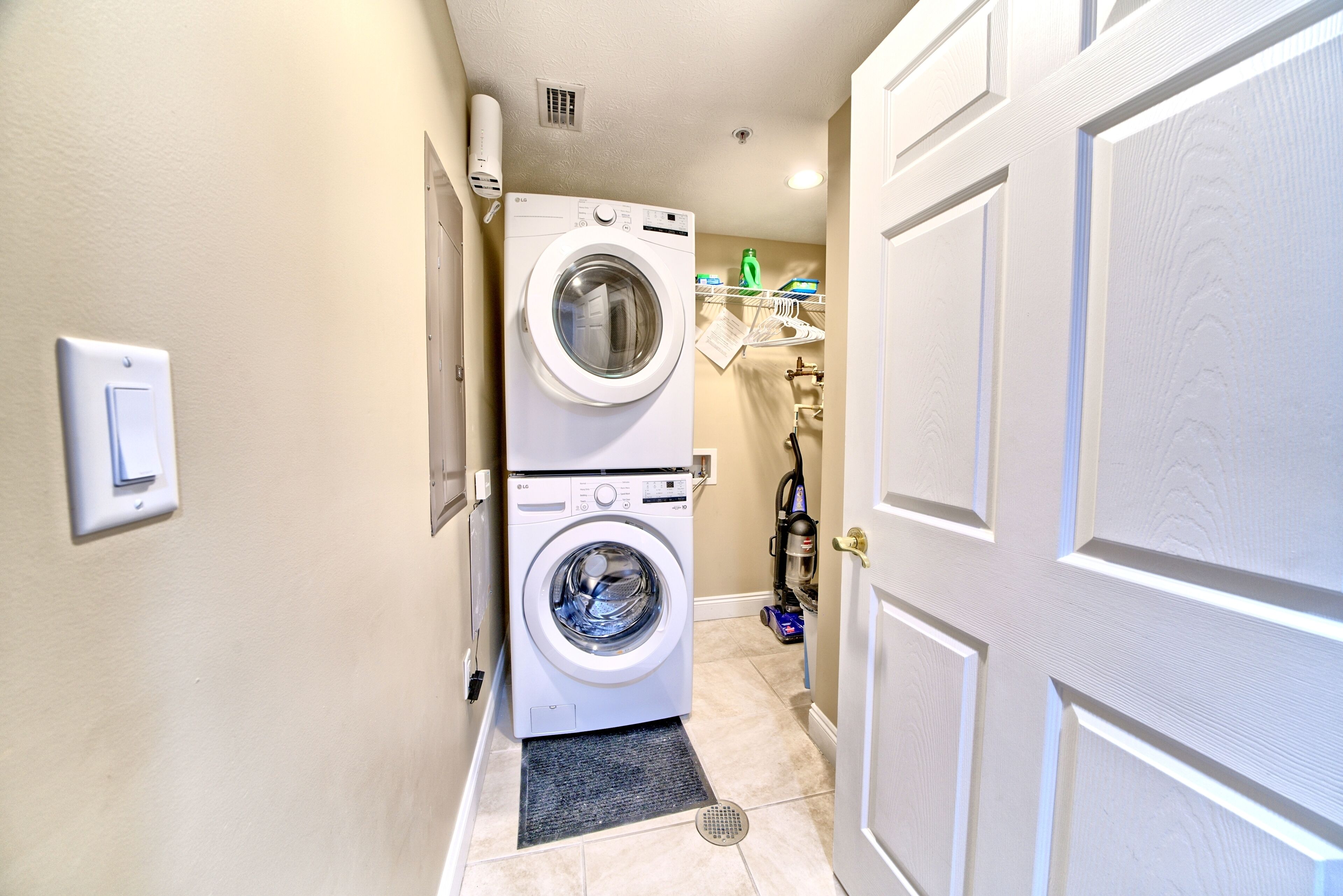 A laundry room with a front-loading washer and dryer, a shelf with cleaning supplies, and a door to the right.