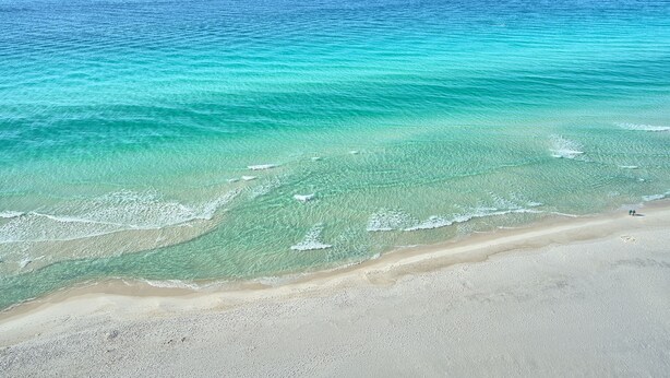 Une plage aux eaux turquoise et limpides, bordée d’un rivage sablonneux.