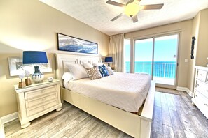 Quarto com cama, mesa de cabeceira, ventilador de teto, janela ampla com vista e porta deslizante para uma varanda.