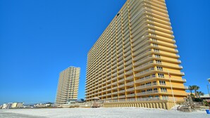Un grand hôtel à plusieurs étages, doté d’une façade uniforme et de balcons, situé près d’une plage.