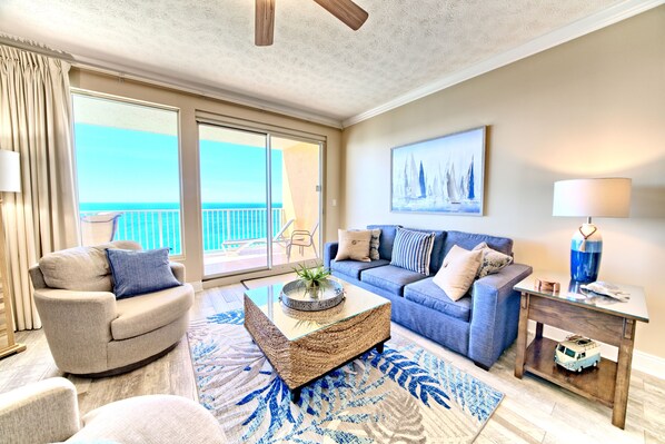 A spacious living room with a large sliding glass door leading to a balcony, a blue sofa, a round coffee table, and a small side table with a lamp.