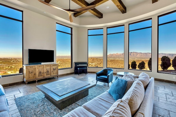A spacious living room with a large TV, comfortable seating, and expansive windows offering a view of the desert. - Ladera Vistas - Panoramic Views, Heated Infinity Pool-Spa, Access to Hiking (Tucson)