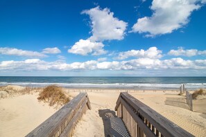 Een houten looppad naar een zandstrand, met de oceaan op de achtergrond.