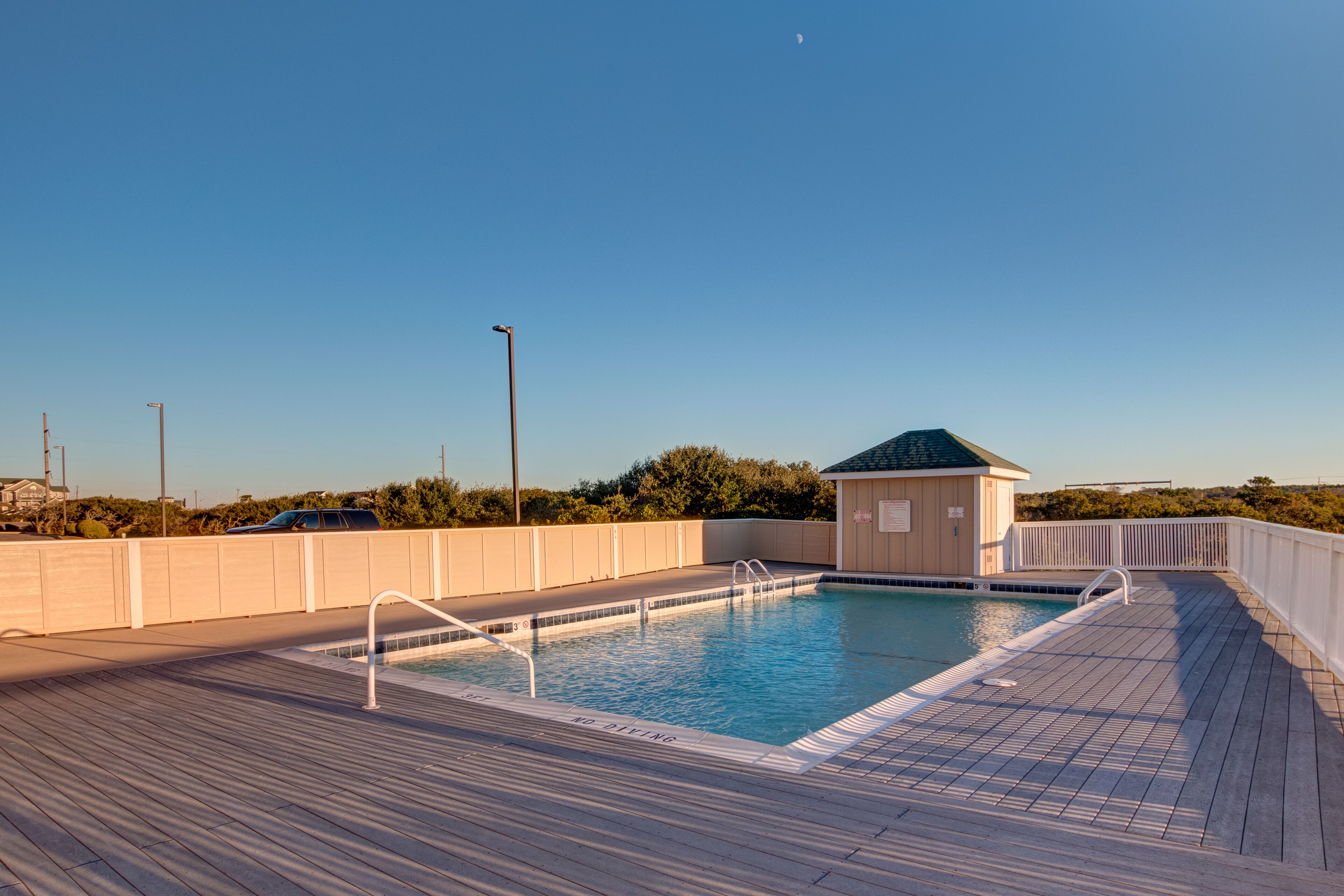 A swimming pool with a wooden deck, a small building with a green roof, and a fence.