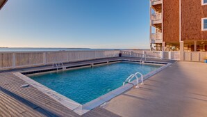 A pool area with a clear view of the ocean, a wooden deck, and a brick building with balconies. - C211-Mary's Heaven - Soundfront Nags Head Condo | Near Beach (Nags Head)