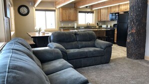 Una sala acogedora con un sofá modular y una cocina con armarios de madera y un refrigerador.