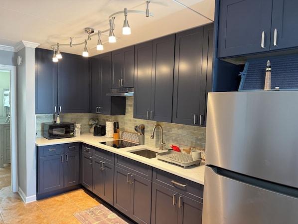 A modern kitchen with dark cabinets, a stainless steel refrigerator, a microwave, and a sink.