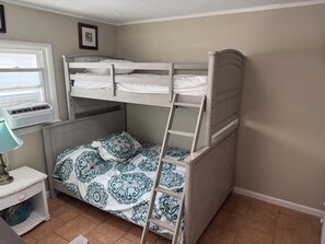 A bunk bed with a ladder, a globe on a shelf, and a window with an air conditioner.
