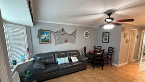 A living room with a dark leather couch, a dining table with chairs, a ceiling fan, and a window with blinds. - Your Summer Escape Awaits!!!  Walking distance to the pristine WWC beaches!!! (Wildwood Crest)