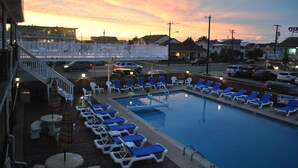 A swimming pool with lounge chairs and a deck area, surrounded by buildings and a sunset sky. - Your Summer Escape Awaits!!!  Walking distance to the pristine WWC beaches!!! (Wildwood Crest)