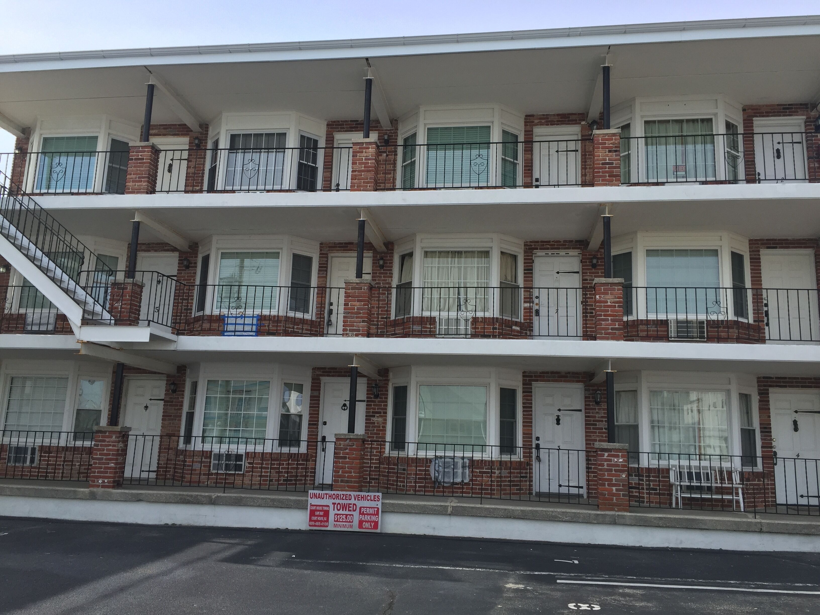 Un edificio residencial de varios pisos con fachada de ladrillo, ventanas con marcos blancos y balcones con barandillas negras.