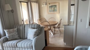 En stue med en stribet sofa, et spisebord med stole, et køkken og et ur på væggen.