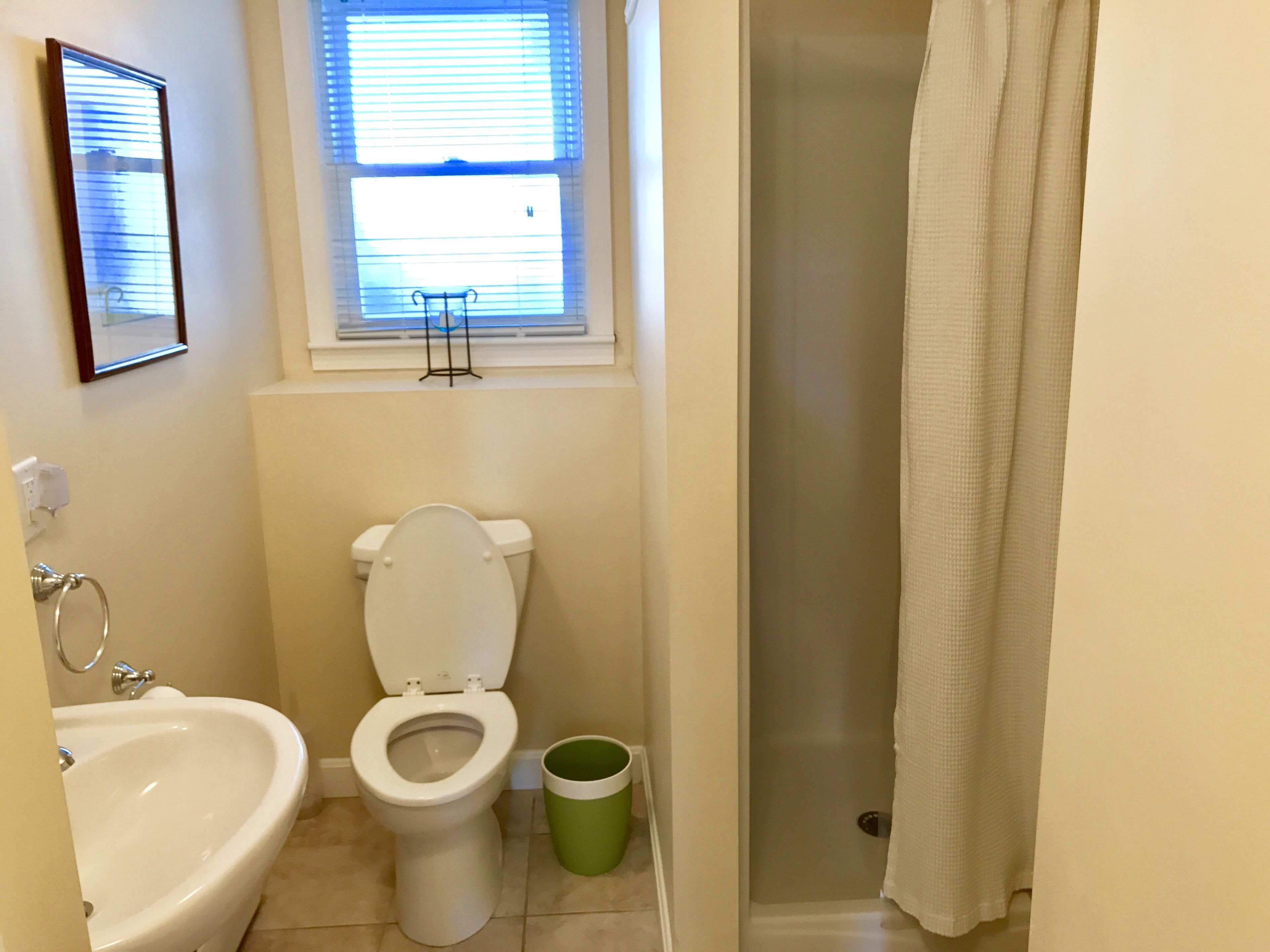 A bathroom with a toilet, bidet, sink, and a window with blinds.