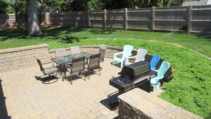 An outdoor patio with a table and chairs, a barbecue grill, and a stone wall. - Central A/C, Walk to Beach, Gated Yard, Wifi, HD TV, Gas Grill, Firepit (West Dennis)