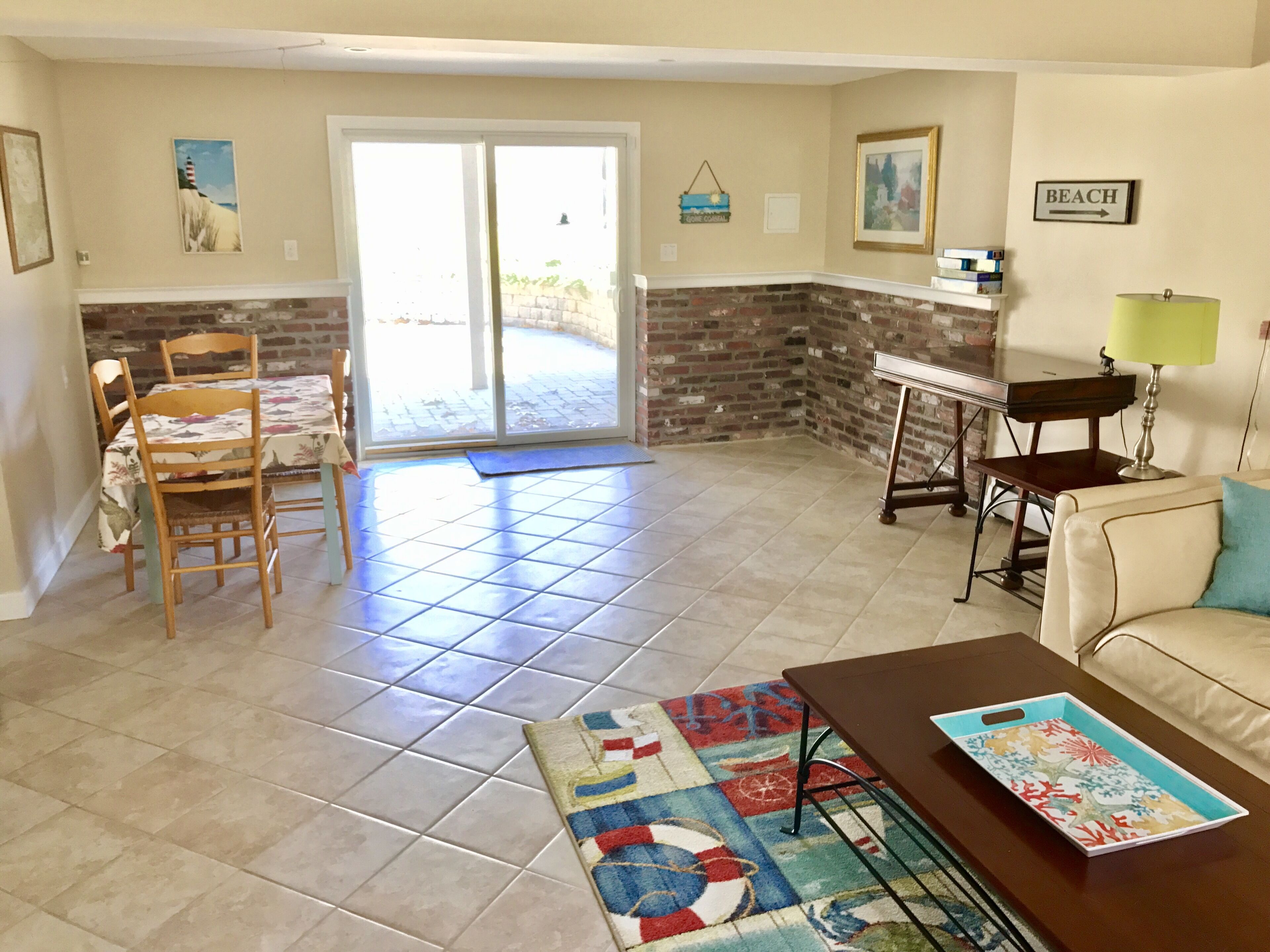A living room with a dining area, a piano, a lamp, and a beach sign.