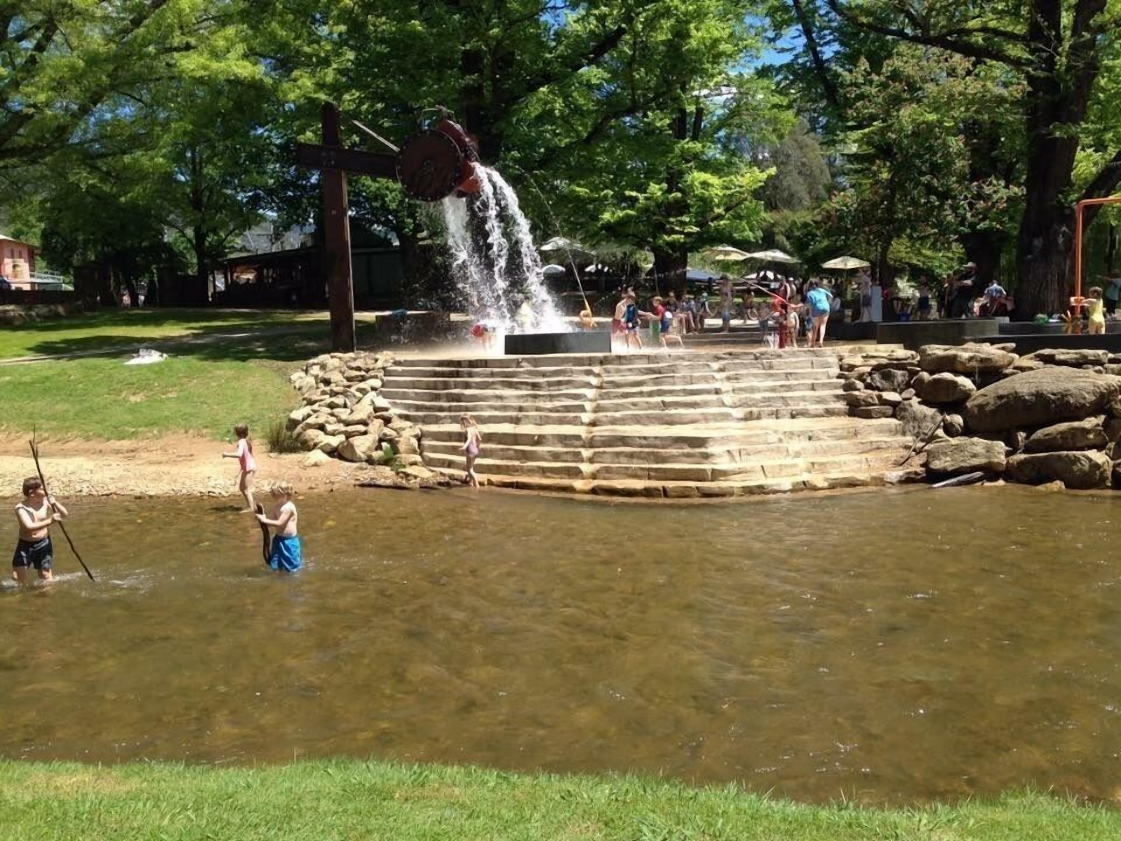 Ein Wasserspiel mit einem stufenartigen Wasserfall und Steintreppen in einer Parkanlage.