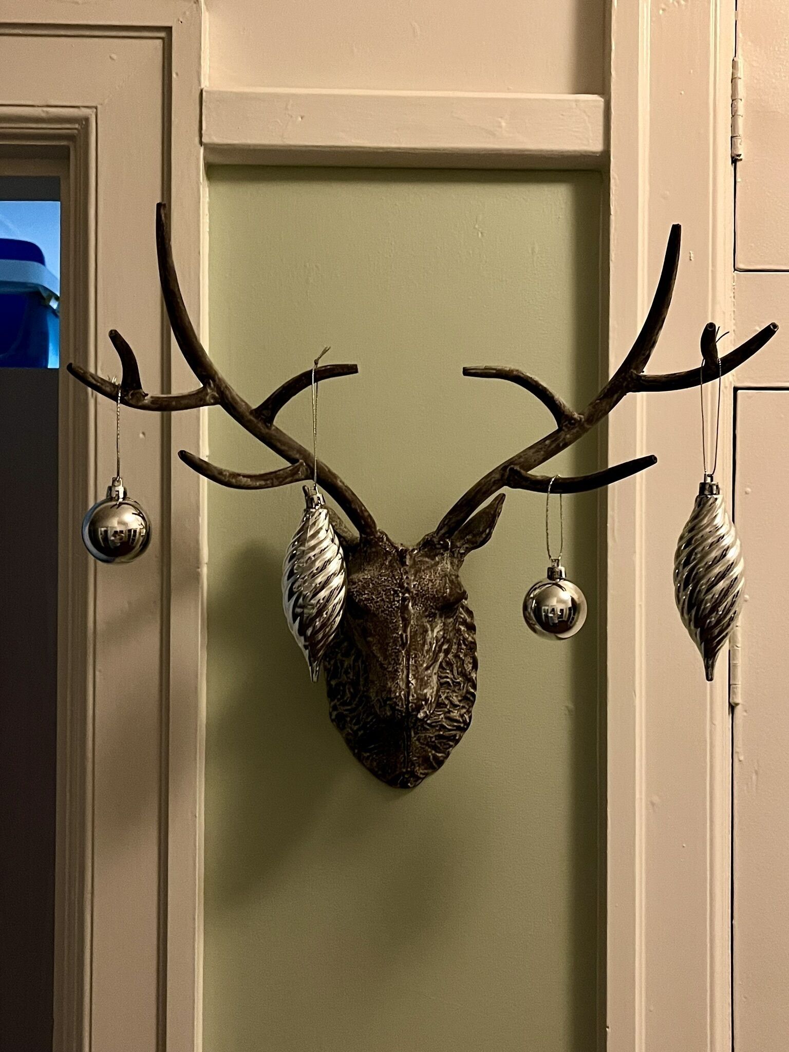 A deer head mounted on a door with antlers and two hanging ornaments.