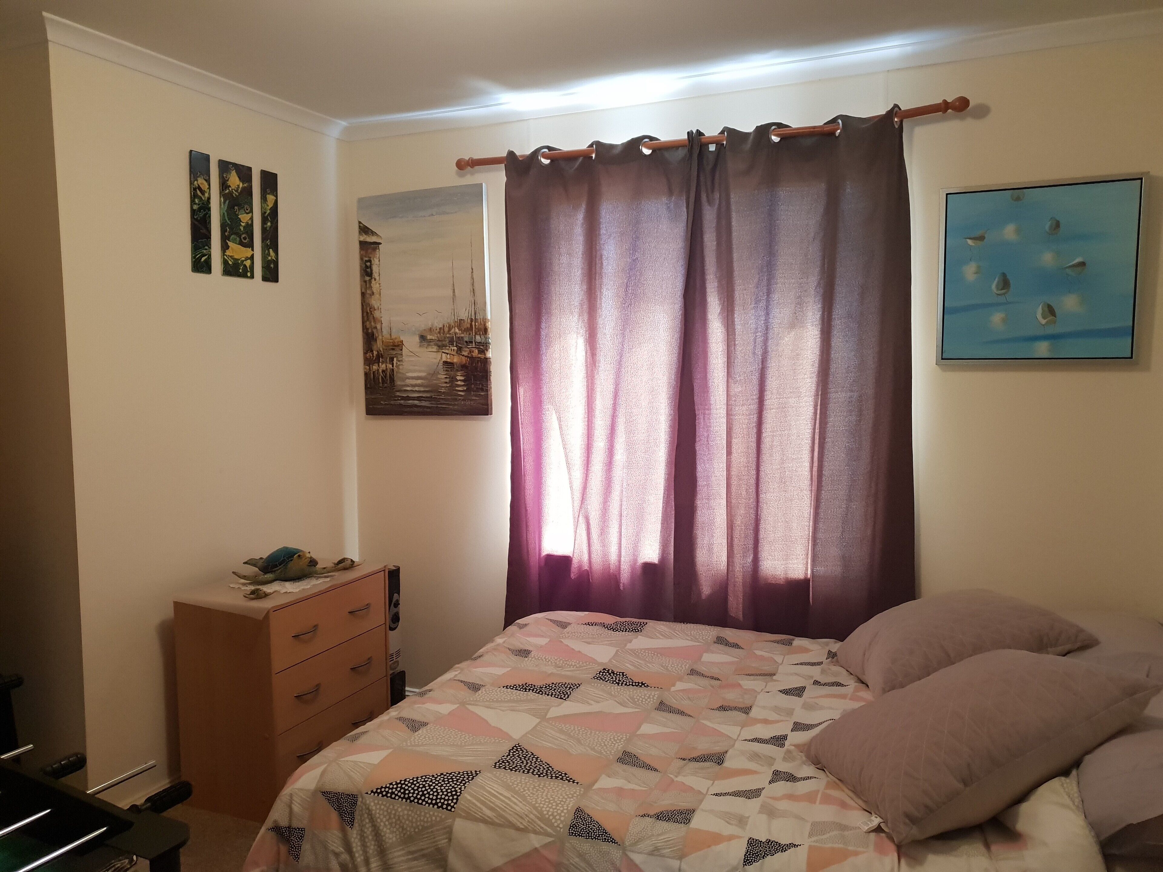 Un dormitorio con una cama, un aparador, un cuadro y una cortina.