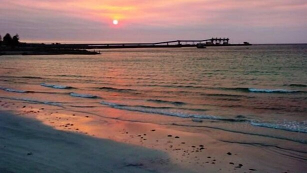 Auringonlasku tyynen meren yllä, ja laiturin pää ulottuu veteen.