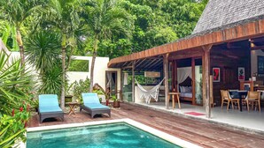 A poolside area with lounge chairs, a hammock, and a covered seating area with a bed and table.