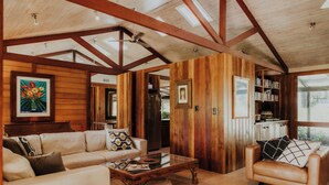A spacious living room with a wooden ceiling, a white sofa, a leather armchair, and a coffee table. - Blue Gum Retreat- Stunning View and Cosy (Bellingen)