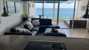 A modern living room with a black leather sofa, a glass-top kitchen island, and a view of the ocean. - Ocean Front In Marbella Assigned underground Parking & fast internet 150 Mbps  (Juan Dolio)
