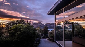 A modern house with large glass windows, a concrete pathway, and a view of mountains and a lake at sunset. - The Loft - Freycinet Holiday houses (Coles Bay)