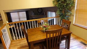 Un comedor con una mesa y sillas de madera, una planta sobre la mesa y una escalera con barandilla.