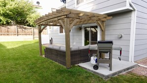 Un patio trasero con una pérgola de madera, una parrilla para barbacoa y una zona de estar integrada.
