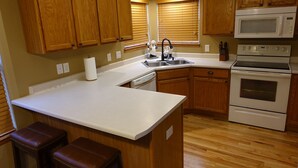 Una cocina con gabinetes de madera, encimera blanca, fregadero, estufa y microondas.