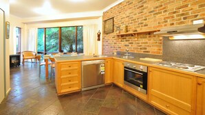 A kitchen with a brick wall, wooden cabinets, a dishwasher, and a stove. - Risehill House
House among tree tops, tranquil and cosy feel. Magnificent views. (Kalorama)